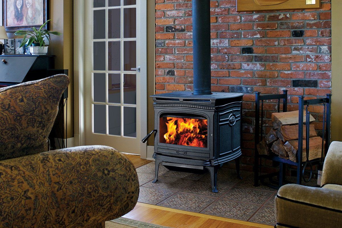 Wood-burning stove with flames in a brick-walled living room. Firewood in a rack, cozy furniture.