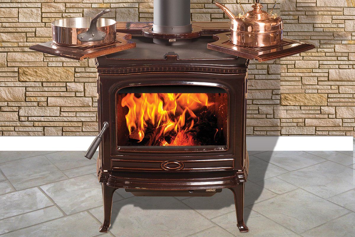 Wood-burning stove with flames, topped with copper pots and trivets, against a brick wall.