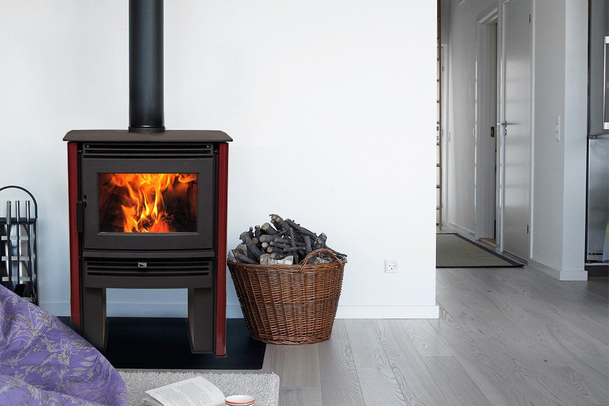 Burning fireplace in a room, with firewood basket and black chimney pipe.