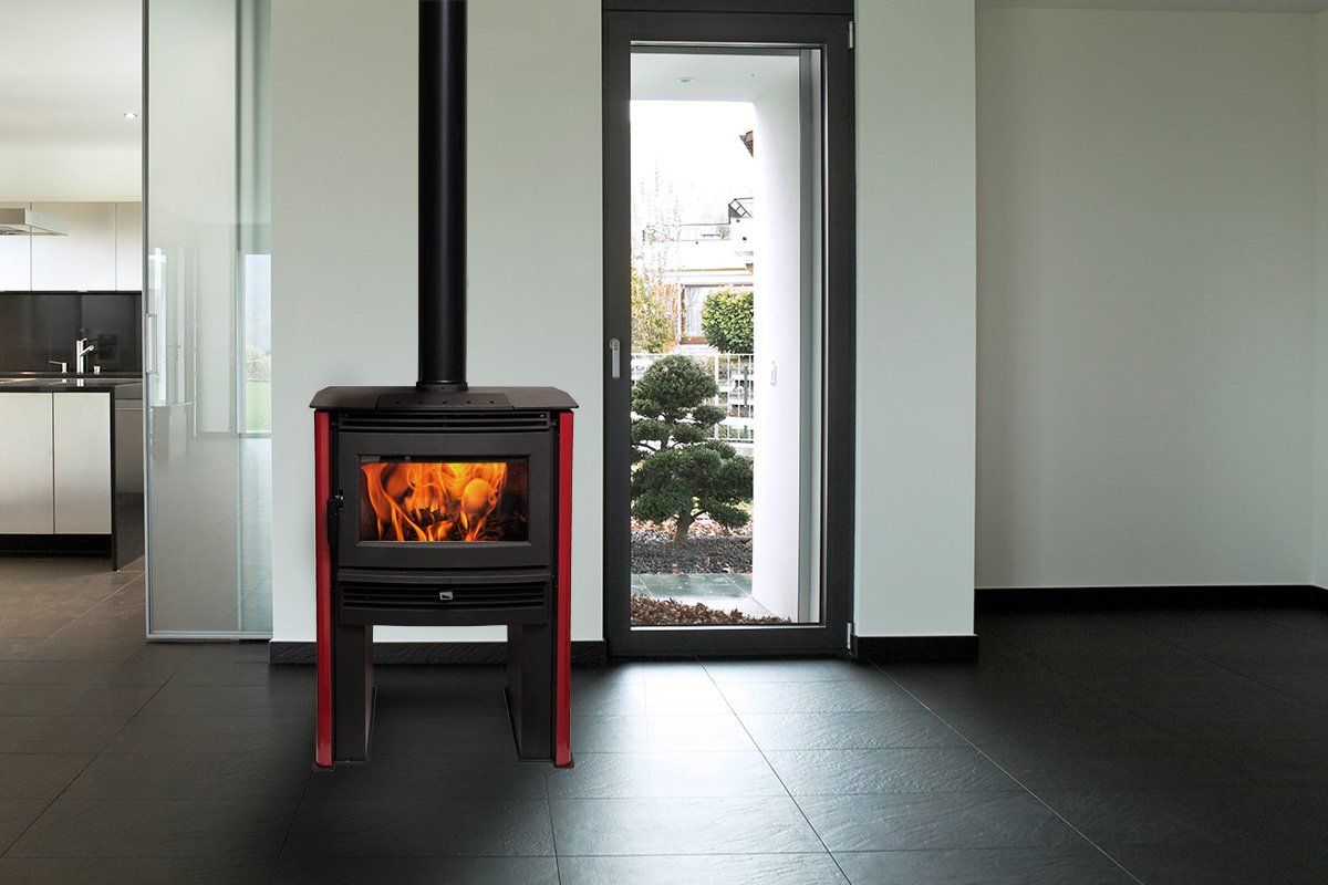 Wood-burning stove with red accents and black chimney in a modern room, flames visible. Doorway with a view.