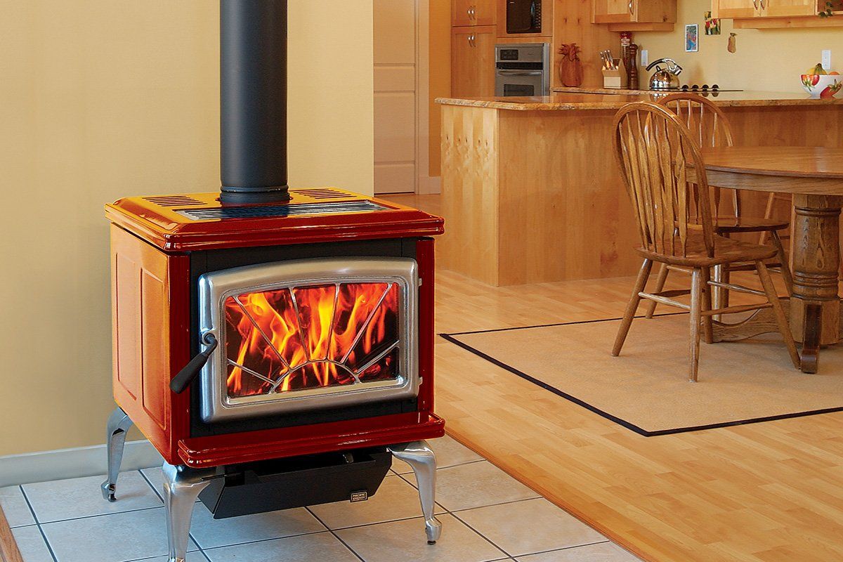 Red wood-burning stove with flames, in a kitchen with wooden table and flooring.
