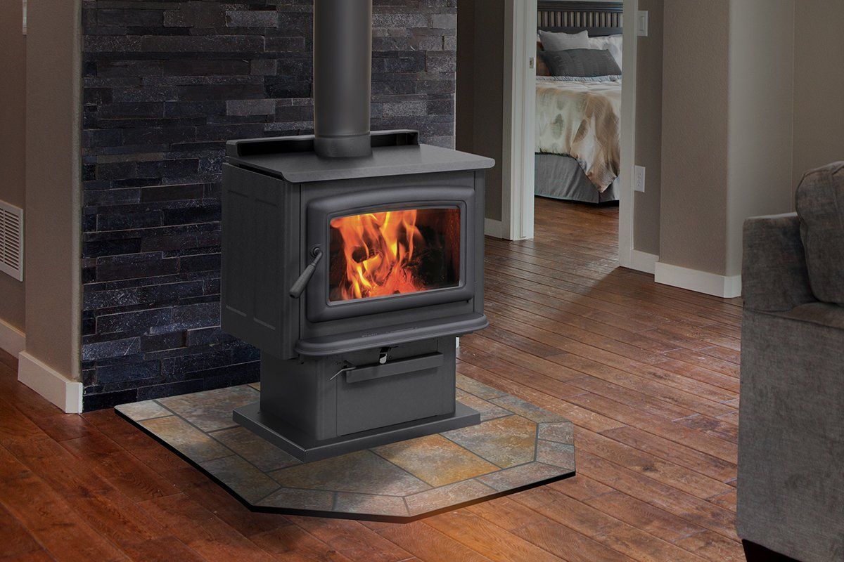 Wood-burning stove with flames, on a tiled hearth. Dark brick wall in the background, hardwood floor.