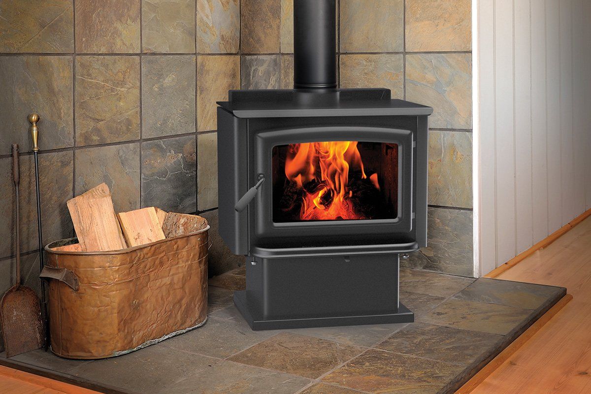 Wood-burning stove with open flames, next to a basket of firewood, set against tiled wall.