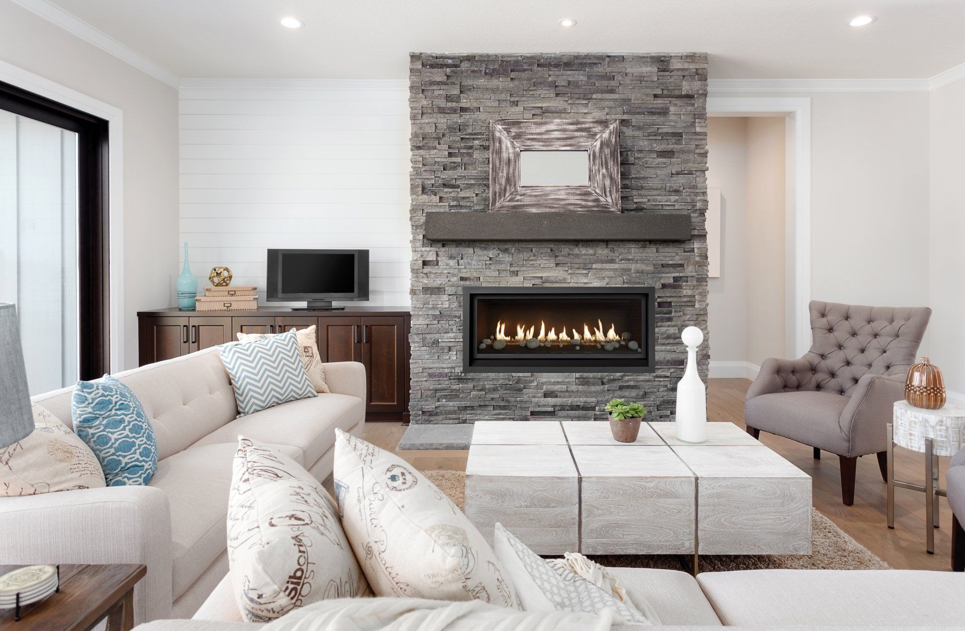 Living room with stone fireplace, beige sofa, TV, and gray accent chair.