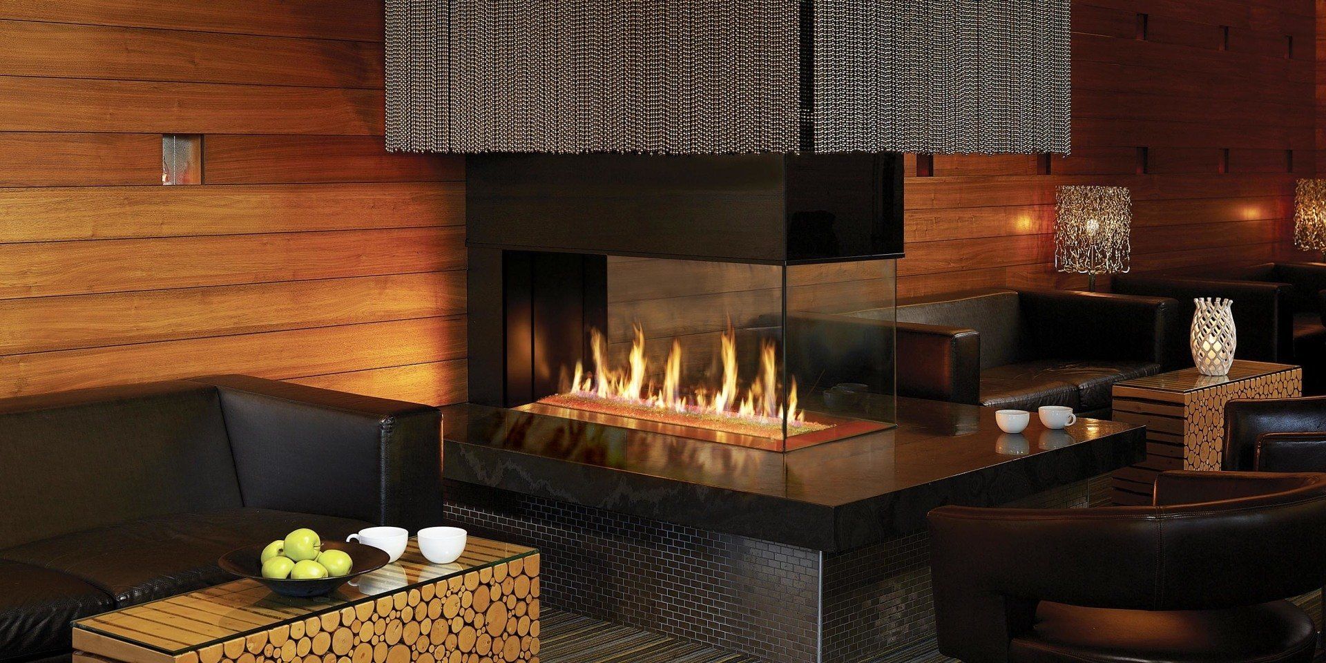 Cozy modern lounge with fireplace and seating. Warm wood paneling and black furniture create a sophisticated ambiance.