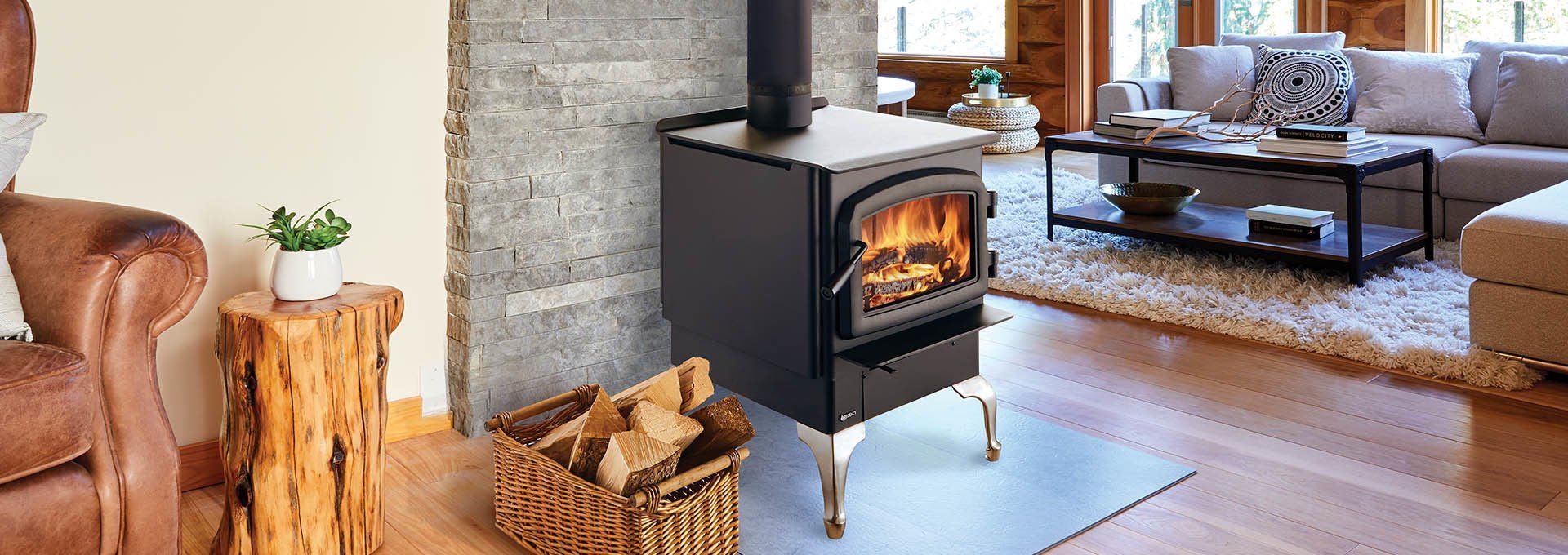 A cozy living room with a lit wood-burning stove, firewood, and a sofa.