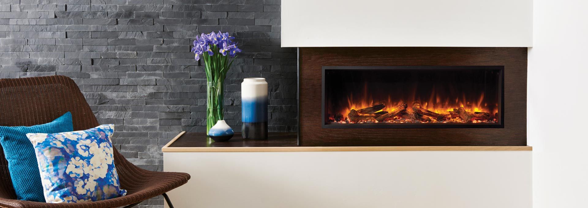 Living room with a fireplace, chair, pillows, flowers, and candles. Dark brown wooden fireplace frame.
