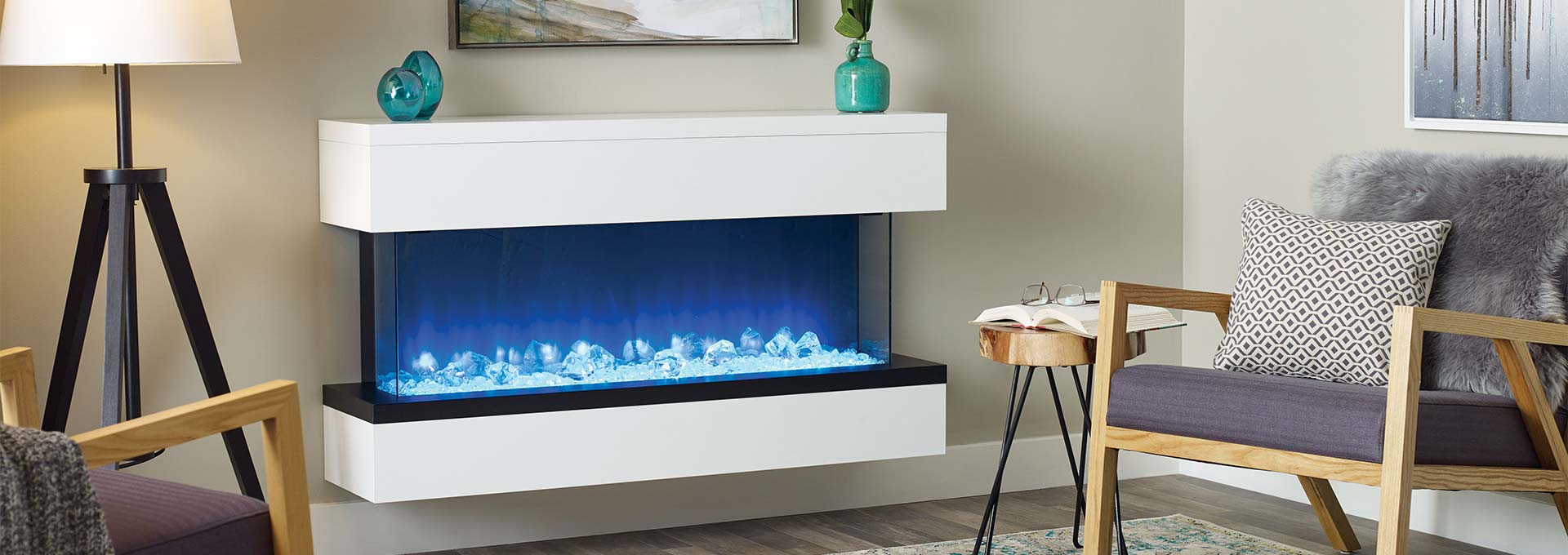 Modern white electric fireplace with blue flame effect, vases and art, chairs, and lamp.