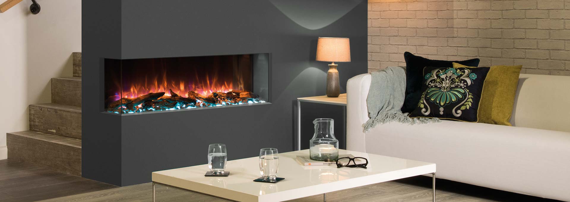 Modern living room with a fireplace, white sofa, and a table with drinks.