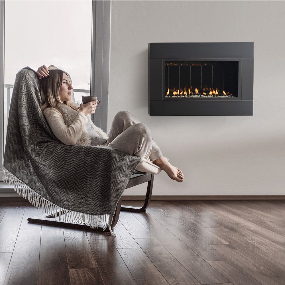 Woman relaxing by a modern wall-mounted fireplace, wrapped in a blanket, holding a mug.