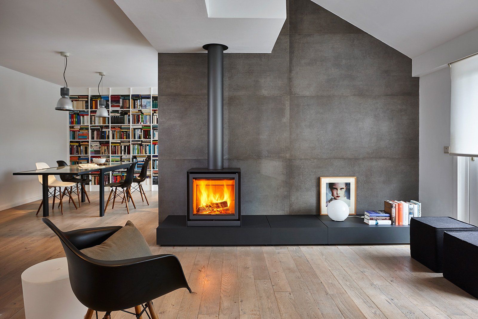 Modern living room with fireplace, bookshelves, dining table, and armchair.
