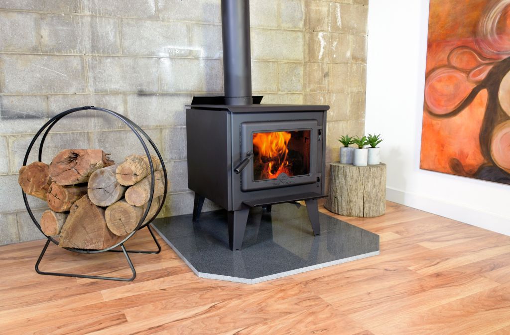 Black wood-burning stove with burning fire, wood pile, and art in a room with hardwood floors.