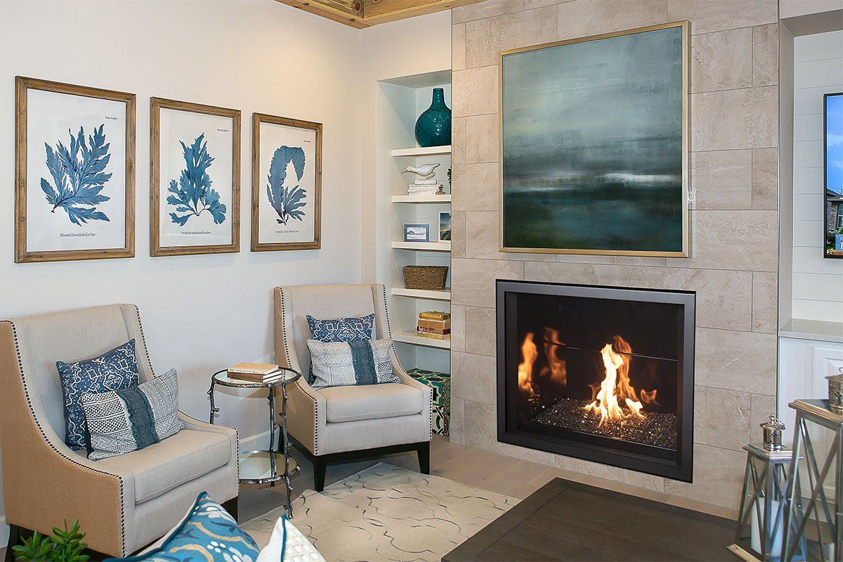 Cozy living room with fireplace, chairs, art, and built-in shelves.  Blues, tan, and white dominate the decor.