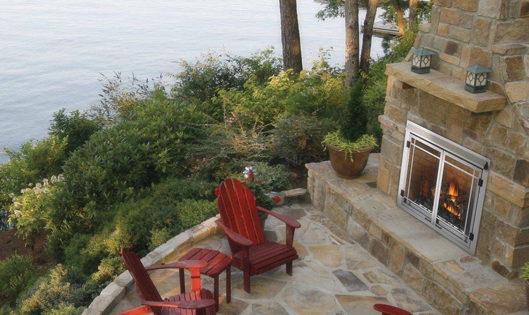 Outdoor stone fireplace with a red Adirondack chair on a patio overlooking a body of water.