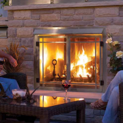 Outdoor fireplace with people sitting by a table, stone wall background. Glowing fire, wine glasses.