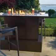 Outdoor fire table with flames, drinks, and a water view.