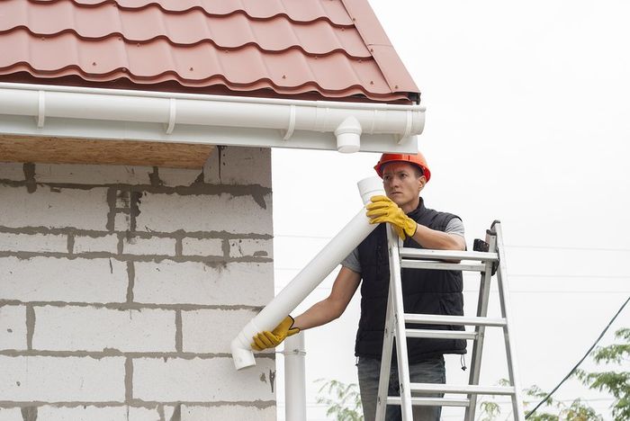 worker on ladder installing gutter pipe