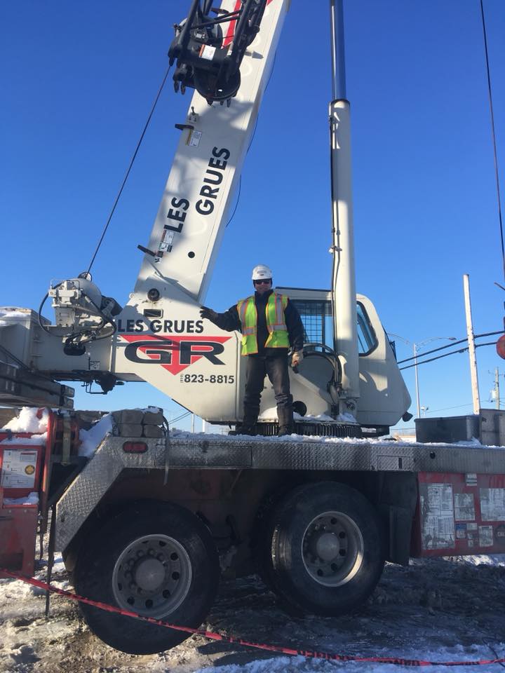 Un ouvrier en gilet fluo sur un camion-grue GRUS sous un ciel bleu azur.