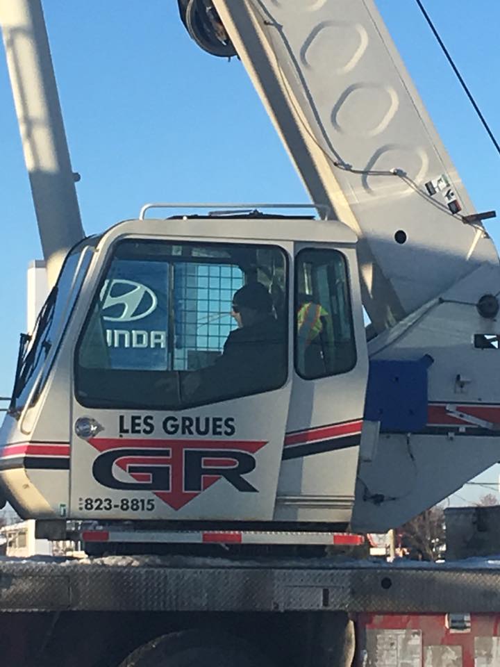 Camion-grue blanc avec logo « GR » et inscription « Les Grues » sur fond de ciel bleu