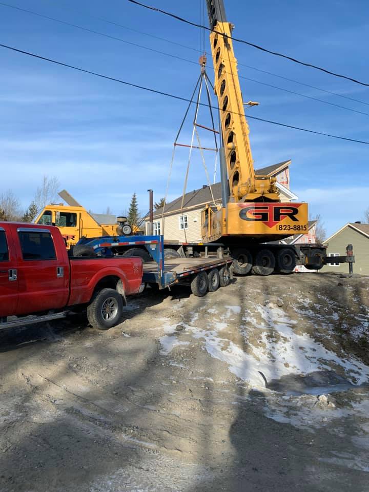 Une dépanneuse rouge soulève une grue jaune sur le bord d'une route enneigée près de maisons