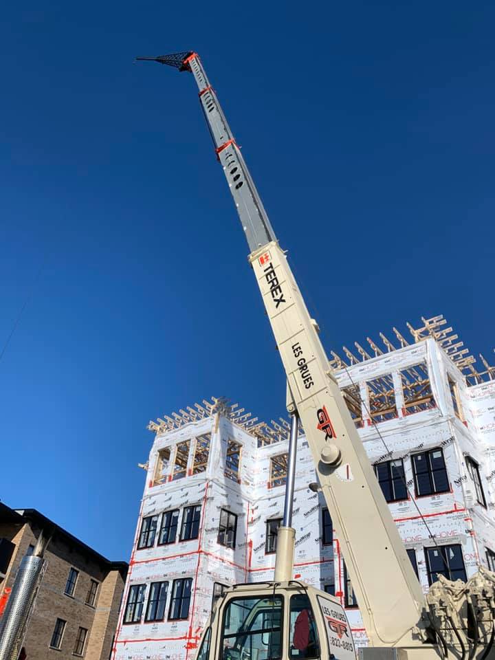 Grue de chantier à côté d'un bâtiment blanc en construction, sur fond de ciel bleu clair