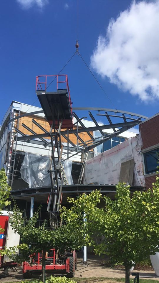 Bâtiment partiellement démoli avec charpente métallique apparente et grue sous un ciel bleu