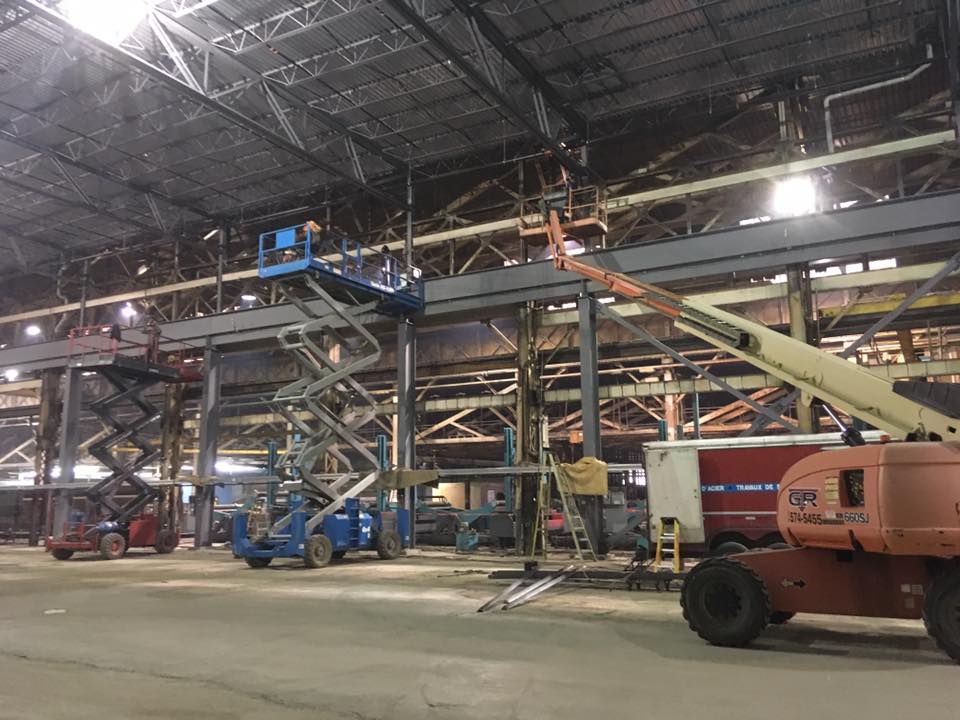 Entrepôt industriel intérieur avec structure en acier et plusieurs chariots élévateurs stationnés sous éclairage de chantier