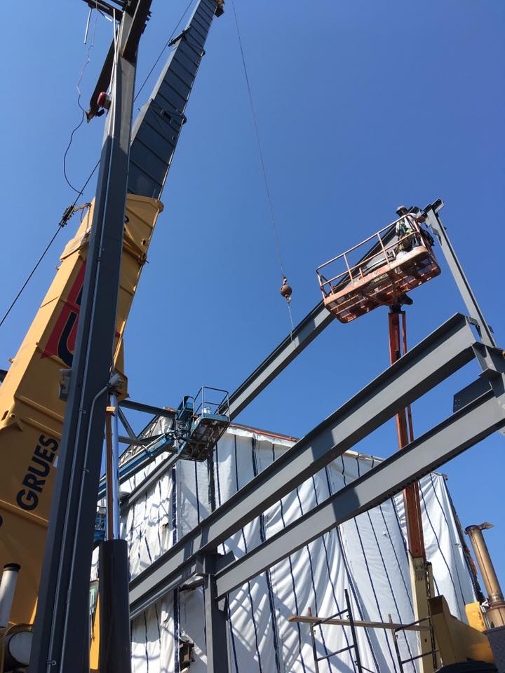 Chantier de construction avec des grues soulevant des poutres d'acier sur fond de ciel bleu clair