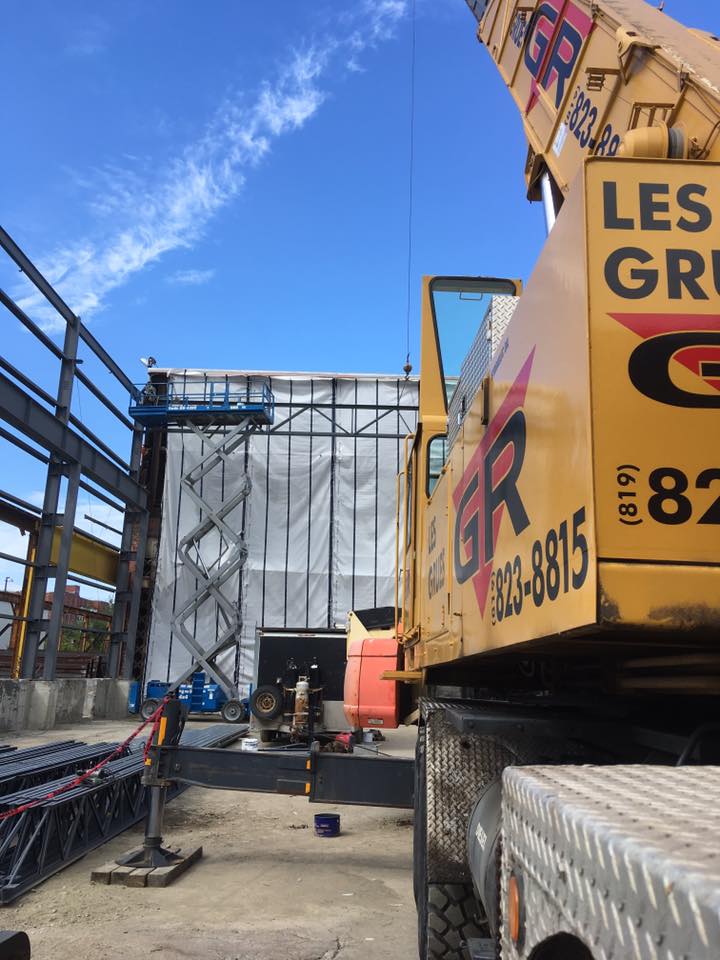 Allée de chantier avec échafaudages, structure couverte et grue jaune sous un ciel bleu