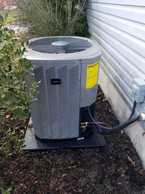 An air conditioner is sitting on the side of a house next to a bush.