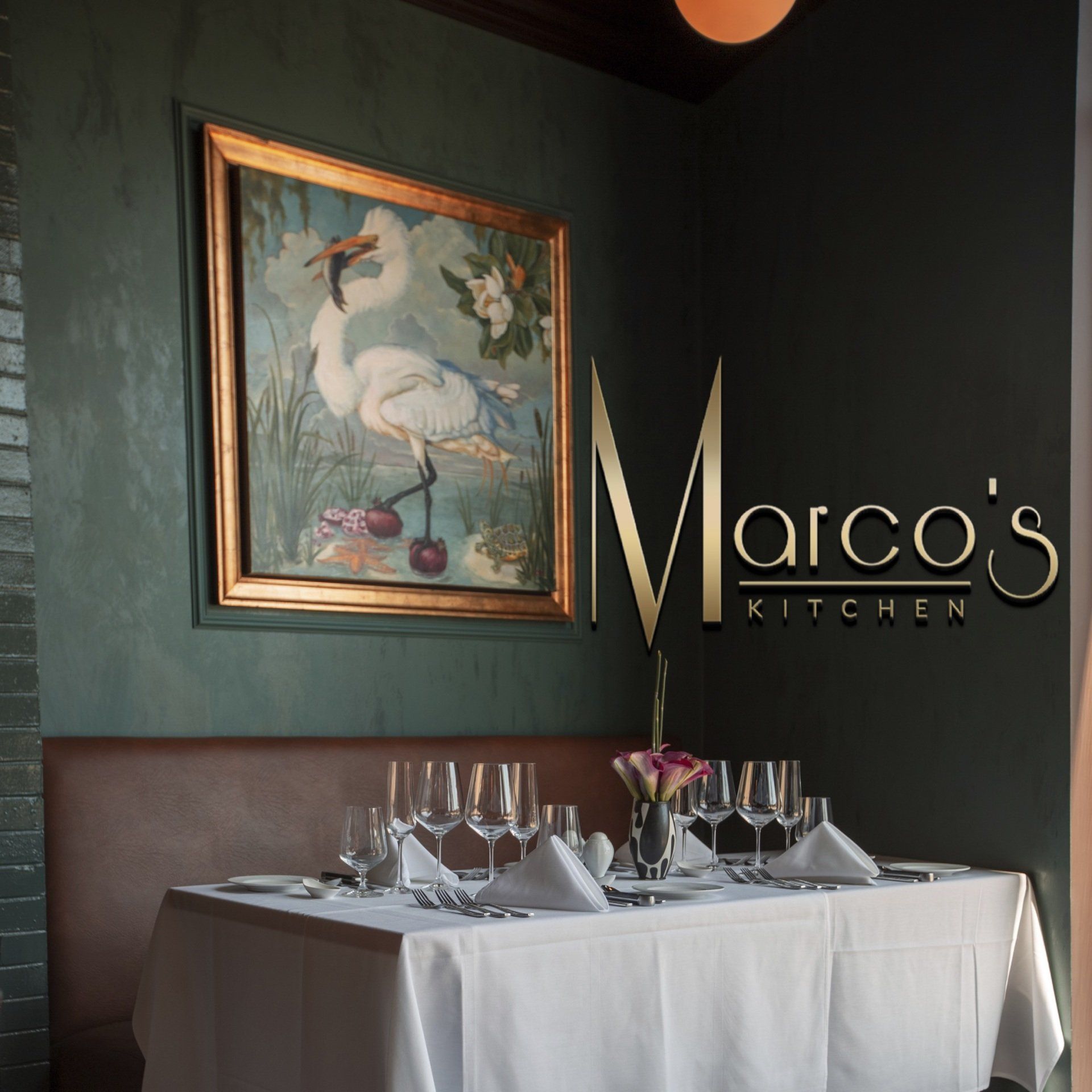 A restaurant called marco 's kitchen has a painting on the wall above the table
