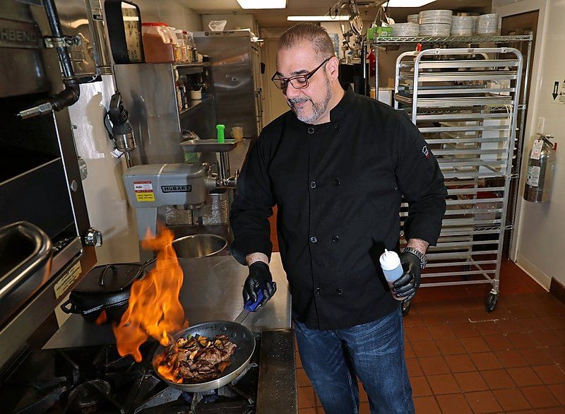 A man is cooking food in a frying pan with flames coming out of it.