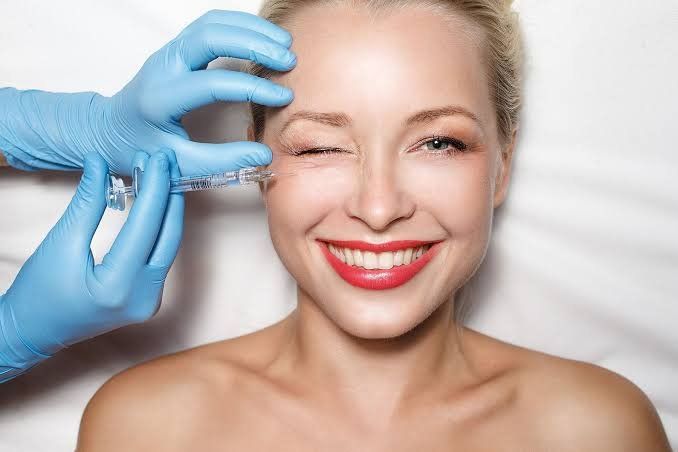 Una mujer sonríe mientras recibe una inyección de botox en la frente.