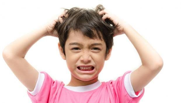 Un niño pequeño se rasca la cabeza mientras viste una camisa rosa.