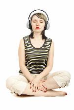 A woman wearing headphones is sitting on the floor with her eyes closed.