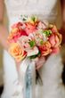 A bride in a white dress is holding a bouquet of pink and orange roses.
