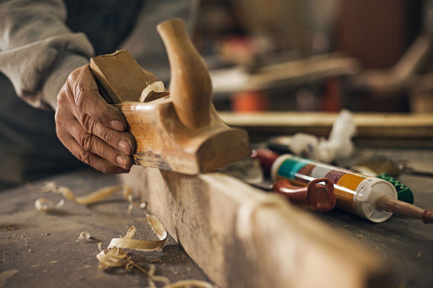 A man is using a wooden plane to plane a piece of wood.
