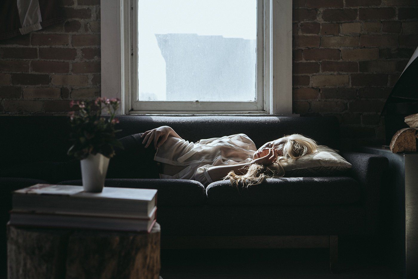 A woman is laying on a couch in front of a window.