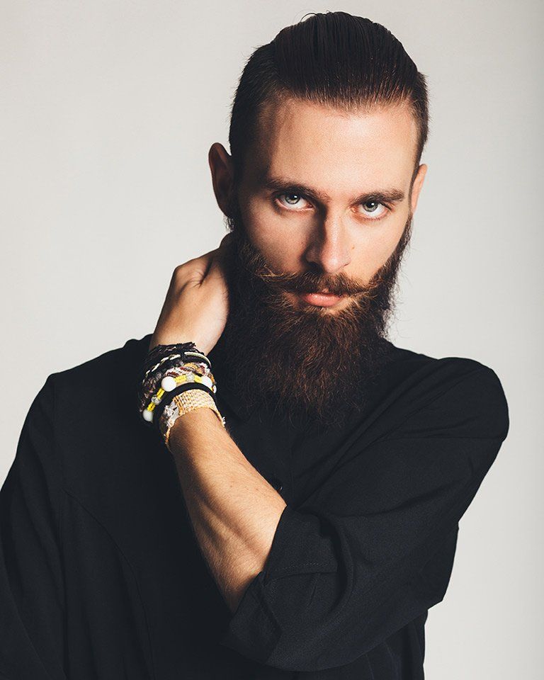 Man with a long beard and mustache, wearing a black turtleneck, holding his neck.