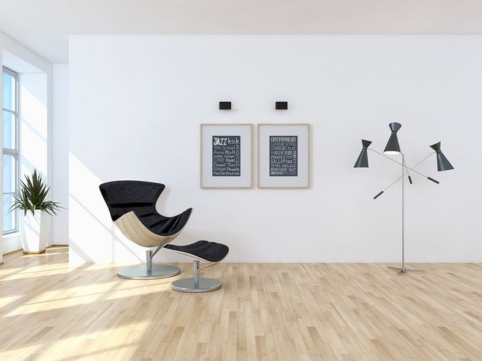 modern chair and footrest in room with two picture frames on wall with modern three headed lamp.