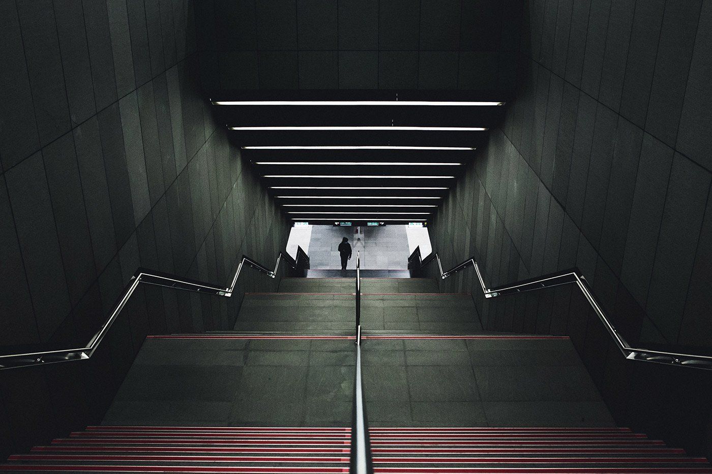 A person is walking down a set of stairs in a dark tunnel.