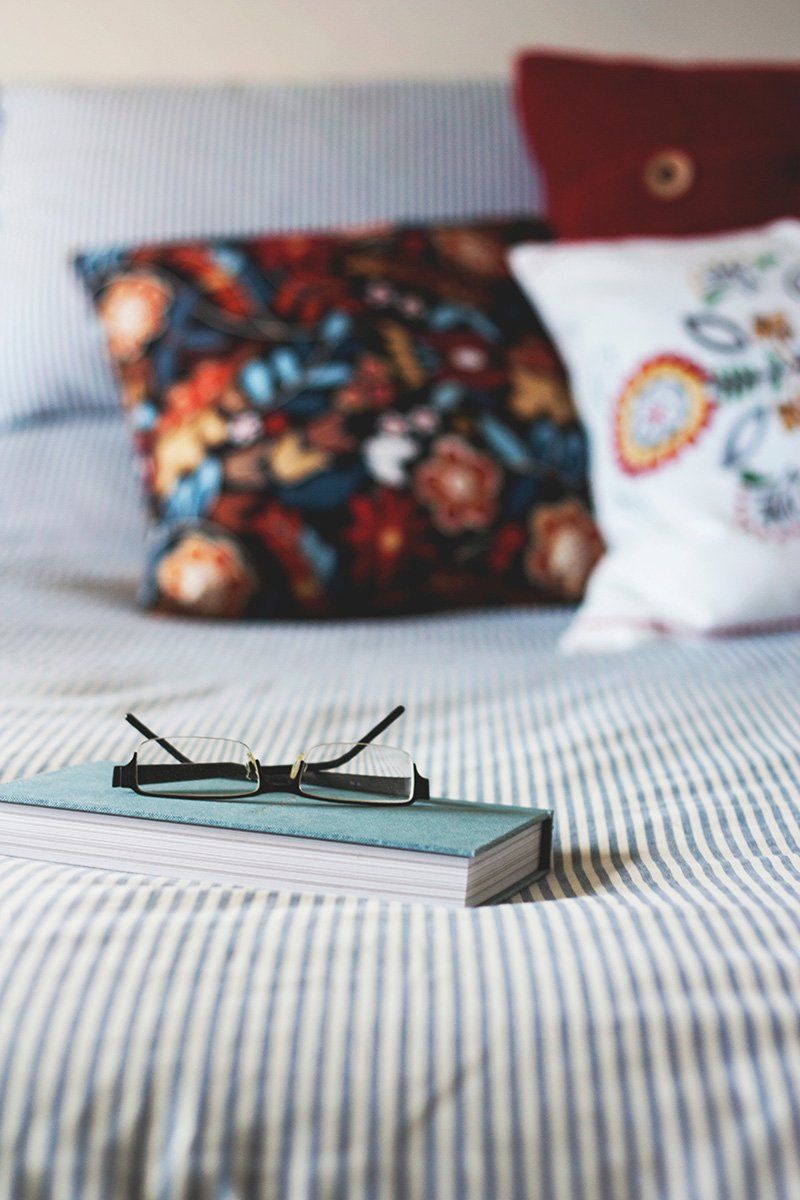 Um livro e óculos estão em uma cama com travesseiros.