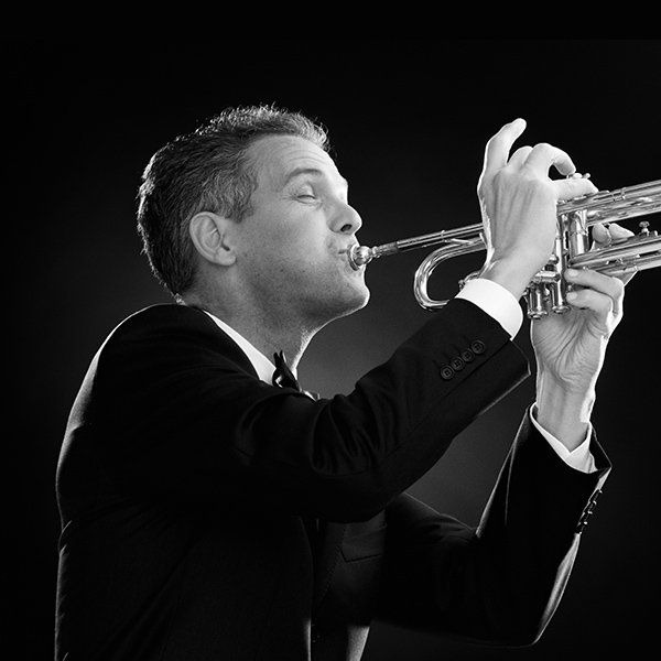 A man in a suit is playing a trumpet in a black and white photo