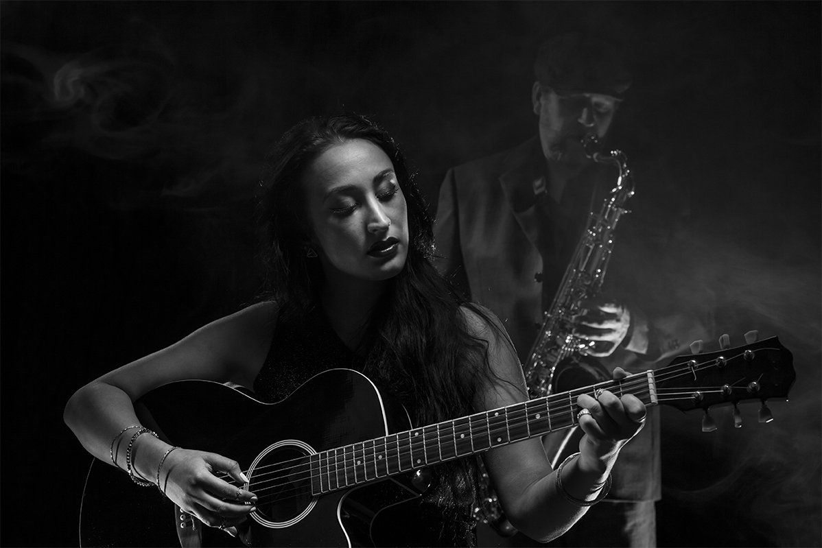 A woman is playing a guitar and a man is playing a saxophone in a black and white photo.