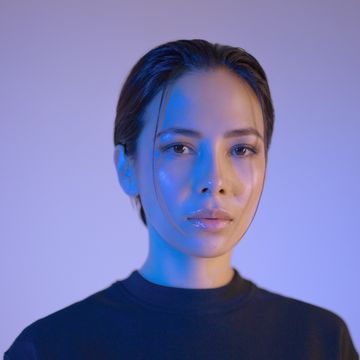 Portrait of a person in blue lighting, wearing a dark top, looking at the camera