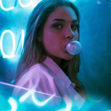 Woman blowing a bubblegum bubble in neon blue and pink lighting