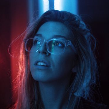 Blue-lit close-up of a person wearing glasses, looking upward against a red background