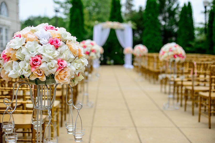 Wedding ceremony aisle with floral arrangements on stands and rows of gold chairs leading to an altar under a white arch.