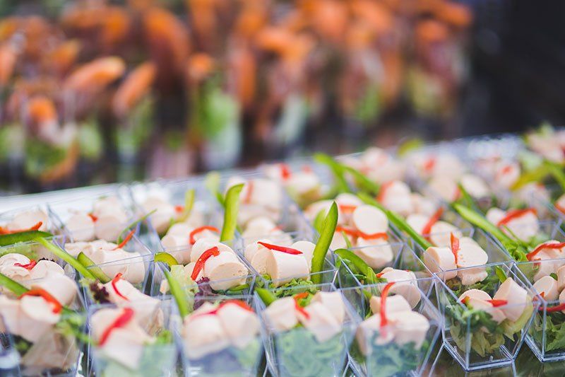 Rows of individual clear plastic cups filled with sliced poultry, fresh greens, and red garnish, arranged for a buffet.
