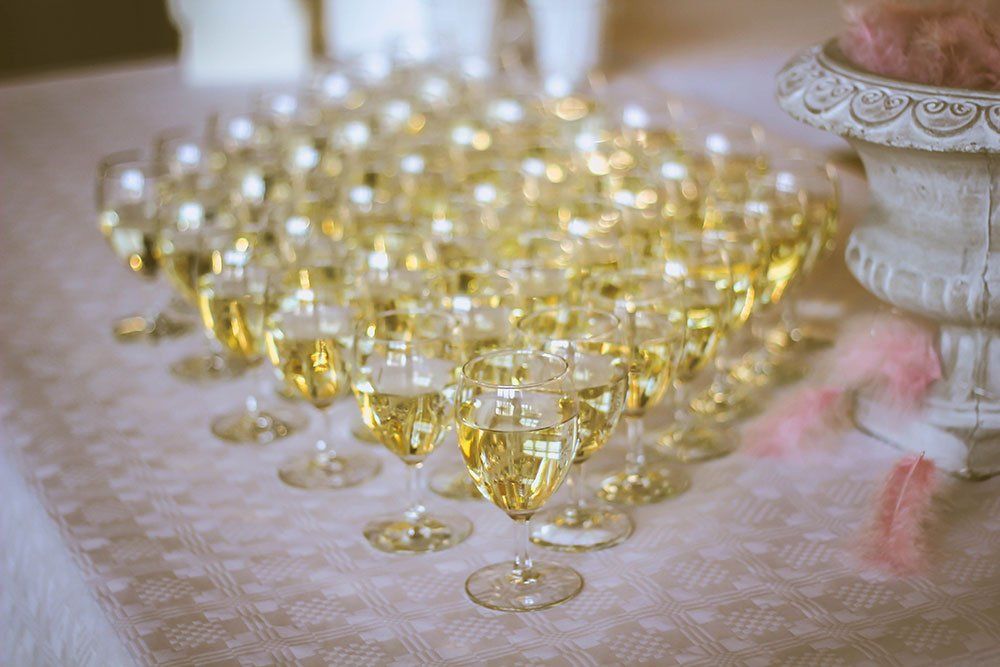 Many glasses filled with golden champagne arranged in neat rows on a table covered with a patterned cloth.
